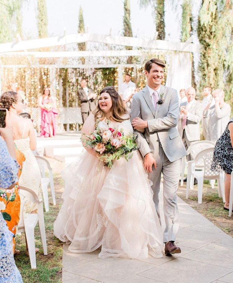 Bride in beige wedding dress walking with groom near guests